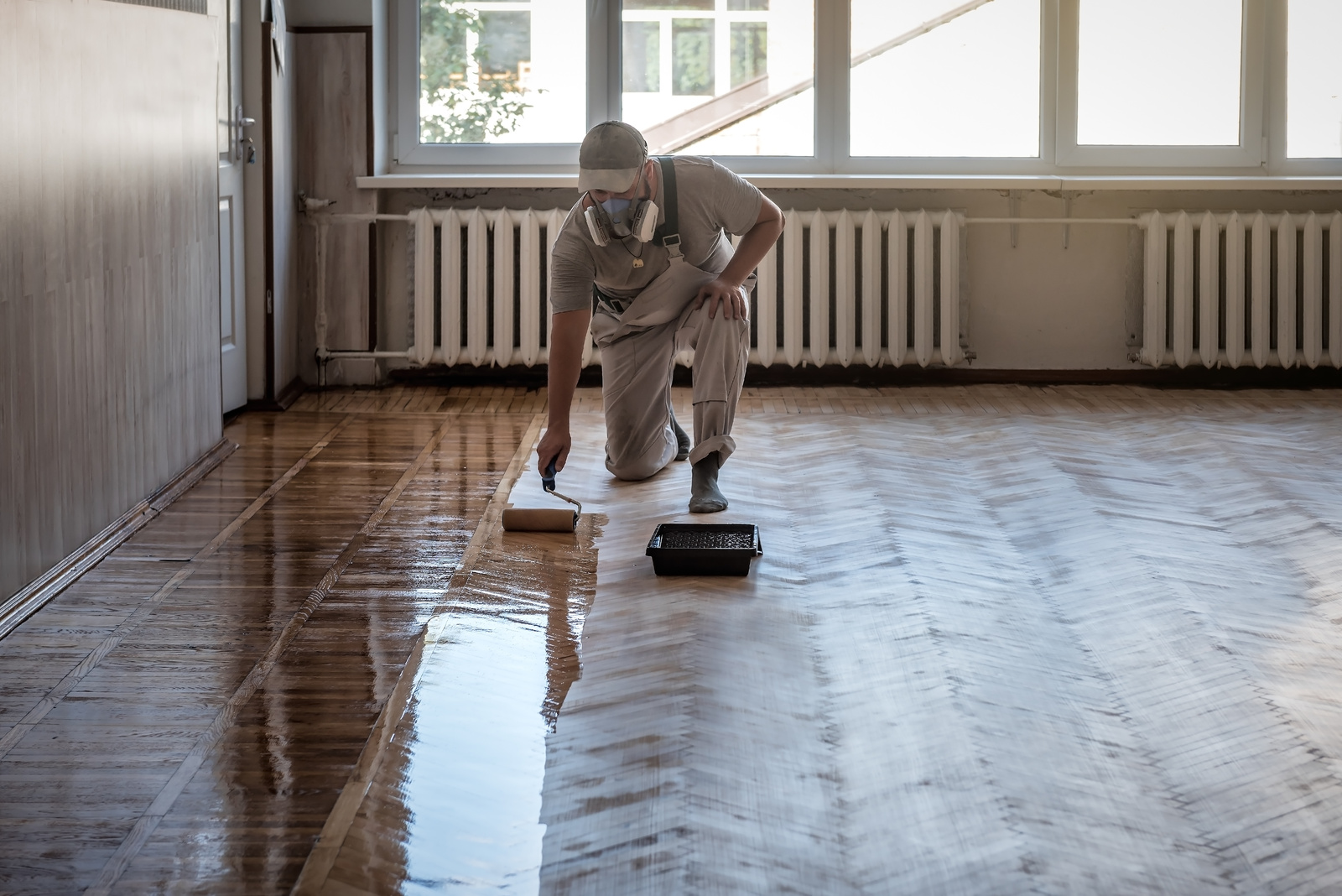 Lacquering parquet floors. Worker uses a roller to coating floors.